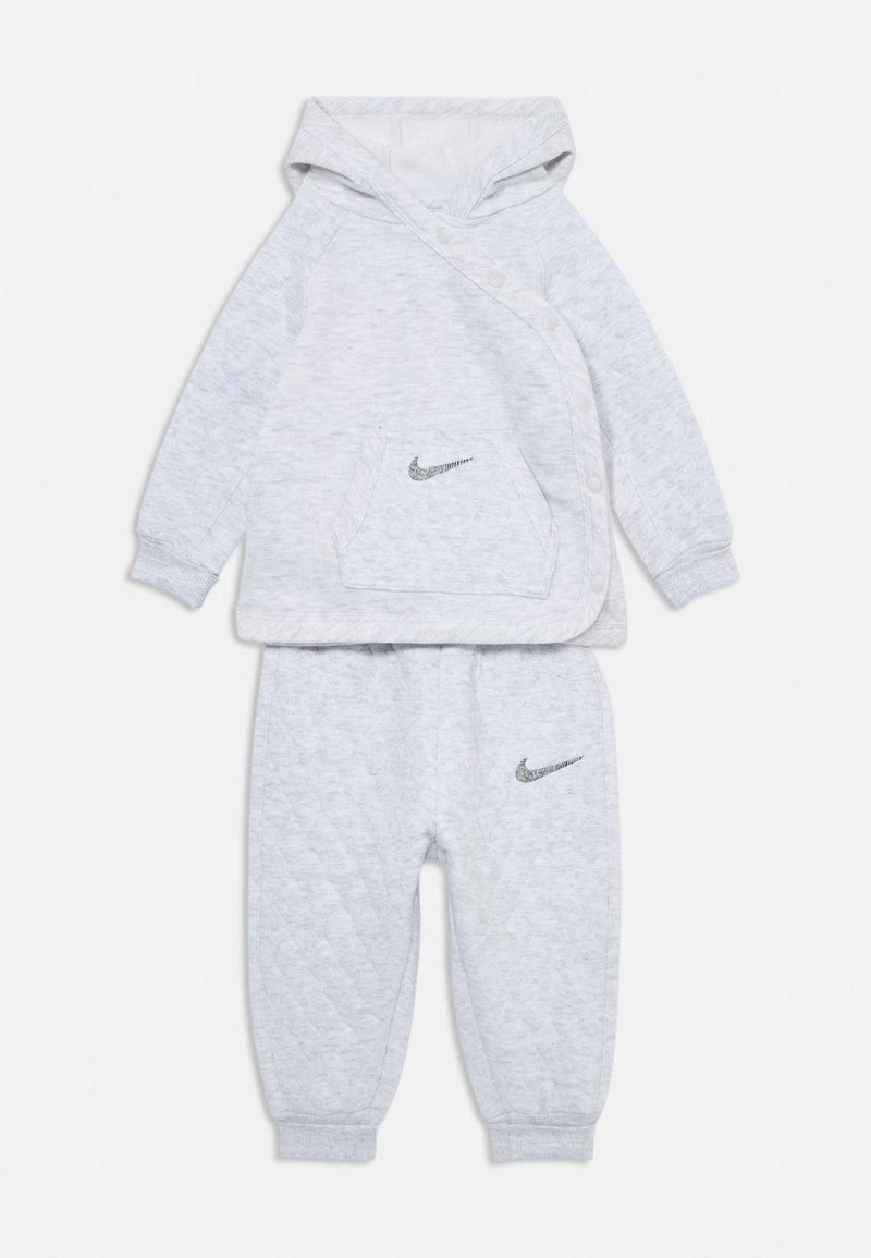 Súprava šedej mikiny a nohavíc z textúrového materiálu, s kapucňou, prednou vreckom a logami Nike na hrudi a stehne.