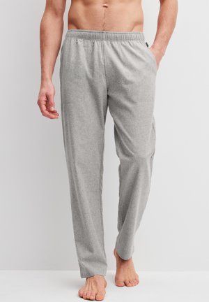 Uomo che indossa pantaloni da casa grigio chiaro con vita elastica, in piedi a piedi nudi su uno sfondo chiaro.