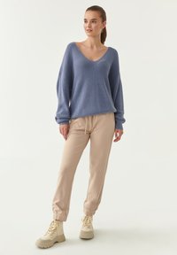 Maglione oversized in azzurro chiaro con scollo a V; abbinato a joggers beige con polsini elasticizzati; stivaletti beige con lacci.