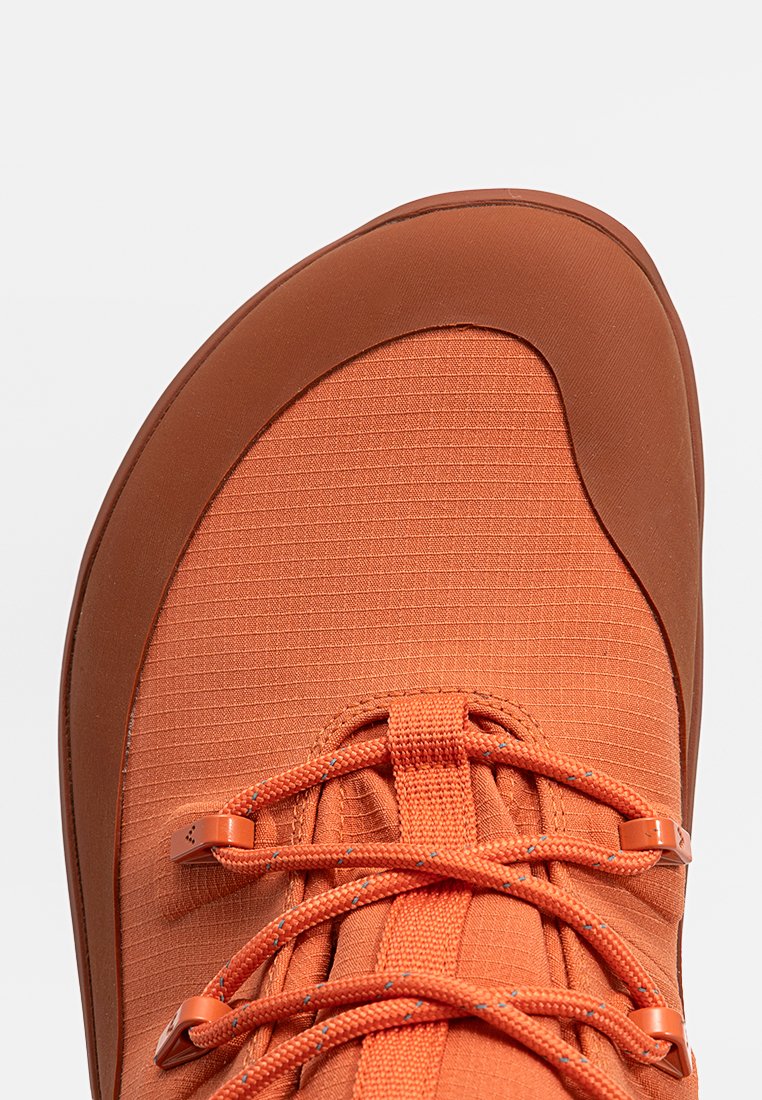 Nahaufnahme der Zehenpartie eines orangen Wander-Schuhs mit strukturiertem Stoff, verstärkter brauner Gummikappe und orangen Schnürsenkeln mit Metallösen.