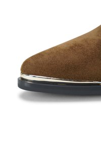 Bruine suède schoen met een spitse neus, voorzien van een zilveren accent langs de zool en een gestructureerd oppervlak.