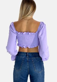Lilla cropped top med smock bagside, flæser ved halsen og ærmer. Parret med højtaljede blå denim jeans. Blødt, tekstureret stof.