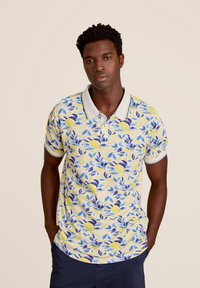 Korte mouwen polo in geel met een bloemenpatroon van citroenen en blauwe bladeren. Witte kraag met blauwe rand, gemaakt van katoen.