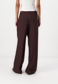Pantaloni largi într-o nuanță profundă de burgundy, confecționați dintr-un material moale cu o textură netedă. Prezintă un talie înaltă și cusături minime.