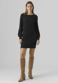 Abito nero a maglia con vestibilità comoda, maniche lunghe a palloncino e scollatura rotonda, abbinato a stivali con tacco in pelle color cammello fino al ginocchio.