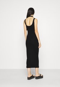 Mustat hihattomat maksimekot, joissa on avoin selkä, vartalonmyötäinen muotoilu, valmistettu sileästä kankaasta, yhdistetty mustiin korokepolkupartioihin.