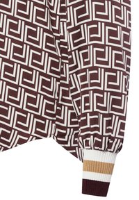 Manica di un indumento con motivo geometrico marrone e bianco, dotata di polsino a coste con strisce bianche, beige e marrone scuro.