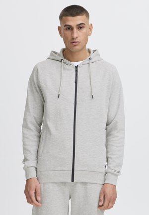 Sudadera con cremallera gris de textura suave, con cremallera negra en contraste y cordones, que presenta un diseño simple y bolsillos tipo canguro.