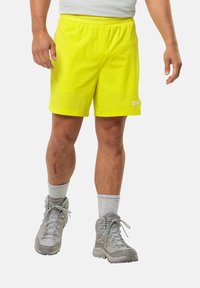 Neon gele lichte shorts met een elastische tailleband, gecombineerd met grijze wandelschoenen en lichtgrijze crew-sokken. Opvallende litteken op het been.