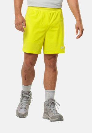 Neon gele lichte shorts met een elastische tailleband, gecombineerd met grijze wandelschoenen en lichtgrijze crew-sokken. Opvallende litteken op het been.
