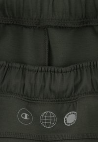 Donkergroene sportkledingstof met een elastische tailleband met gestikte randen en bedrukte logo's in lichtgrijs.