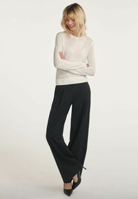 Kremowy sweter z długim rękawem w połączeniu z czarnymi spodniami o szerokich nogawkach i czarnymi szpilkami. Strój charakteryzuje się luźnym krojem i prostym wzornictwem.