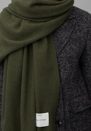 Écharpe en laine vert foncé avec une étiquette blanche affichant la marque et le texte laine recyclée, portée sur un manteau texturé gris foncé.