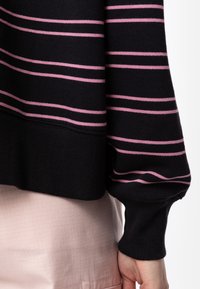 Jersey negro con rayas horizontales rosa, puños y dobladillo acanalados. La tela parece suave y con un ajuste relajado. Se ve una falda rosa clara texturizada.
