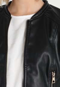 Zwarte leren bomberjack met een zachte textuur, voorzien van een geribde kraag, zilveren rits en een zijzak met een ritssluiting.