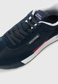 Sneaker blu navy con strati in suede e mesh, dettagli bianchi, lacci piatti e una toppa con il marchio sulla linguetta, che mostra un design a bassa altezza.