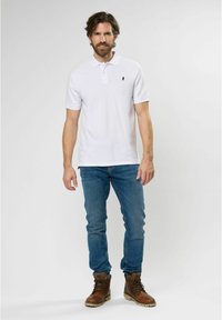 White polo shirt with a collar and three buttons, paired with blue jeans and brown lace-up boots. Simple design, soft texture.