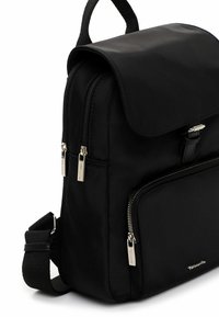 Mustast nailonist seljakott klapiga kinnitusega, kahe esiosa tõmblukuga ja küljes rihmaga. Omab läikivaid hõbedaseid metallosad ning elegantset, minimalistlikku disaini.