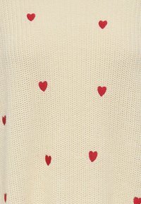 Tissu en maille crème avec de petits cœurs rouges brodés, répartis de manière homogène sur toute la surface.