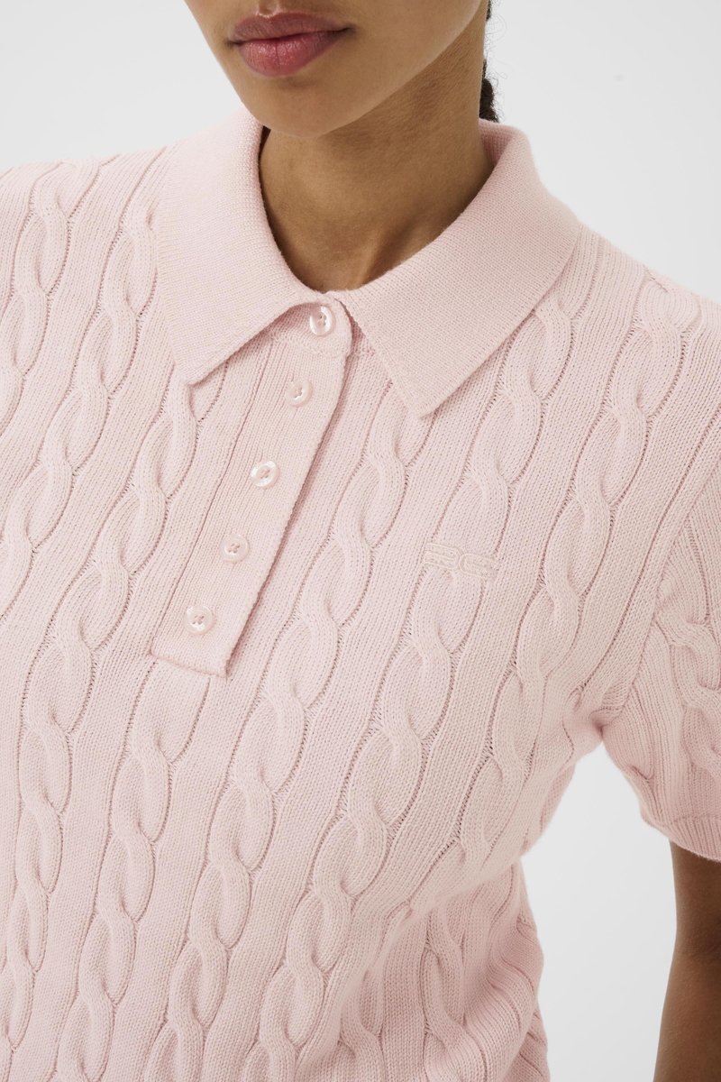 Femme portant un polo en maille torsadée rose clair à manches courtes avec une patte boutonnée et un col à revers.