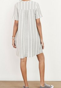 Robe à manches courtes rayée en tissu gris clair et blanc, avec une coupe décontractée et un dos froncé. Portée avec des baskets grises.