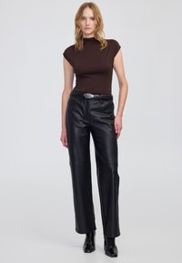 Maglione a collo alto marrone aderente abbinato a pantaloni ampi in pelle nera a vita alta e stivaletti neri, con vita cinturata.