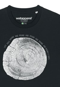 Schwarzes T-Shirt mit einem weißen bedruckten Baumringdesign, das kreisförmige Wachstumsringe und den Satz "DAS LEBEN DREHT SICH RUND UND RUND UND RUND GEHT ES." zeigt.