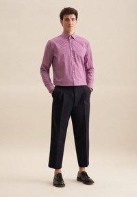 Camicia a righe rossa e bianca con colletto a punta, abbinata a pantaloni larghi blu scuro e scarpe nere con lacci.