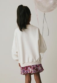 Overdimensioneret cremet sweatshirt med ribbede manchetter, parret med en pink og lilla palietternederdel. Balloner med pastelribbons er til stede.