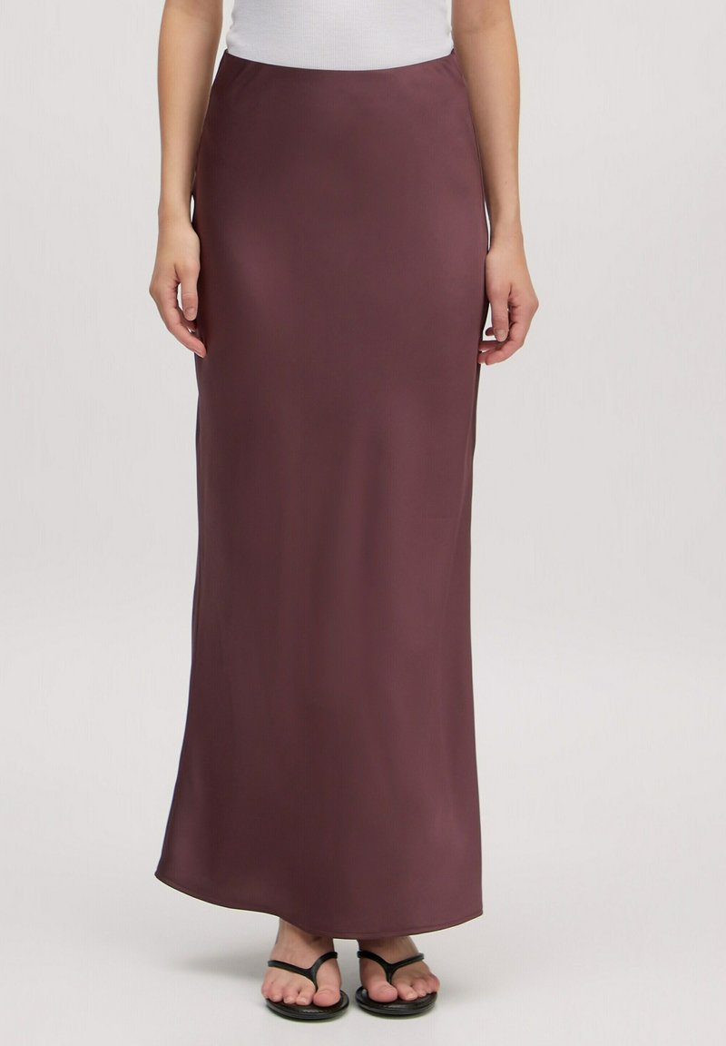 Maxi rok in diep bordeauxrood, gladde textuur, aansluitende taille, enkel-lang, gecombineerd met zwarte slippers voor een casual look.