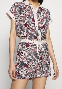 Bloemrijke korte mouw jumpsuit in lichte stof met rode en marineblauwe patronen, knoopsluiting aan de voorkant en een trekkoord in de taille voor een verstelbare pasvorm.