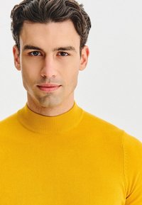Żółty sweter z golfem o prążkowanej strukturze, dopasowany do sylwetki, wykonany z miękkiego materiału, podkreślający gładką fakturę i elegancki krój.