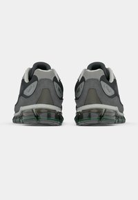 Atlétikai cipő szürke hálós és velúr felsőrésszel, zöld díszítésekkel, párnázott szegéllyel és átlátszó gél talppal a párnázás és a támogatás érdekében.