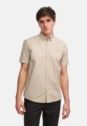 Camisa de manga corta color beis hecha de algodón, con cuello abotonado, botones en la parte delantera y un pequeño logo bordado en el pecho.