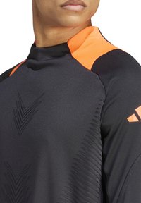 Zwart sportshirt met een oranje kraag en schouderaccenten. Heeft gestructureerde patronen aan de voorkant en een slank, getailleerd ontwerp.