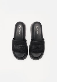 Black DKNY slide sandals with a textured mesh strap and a smooth rubber sole. Feature embossed branding on the strap and footbed.