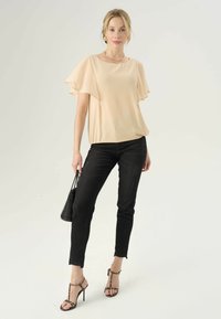 Beige, vloeiende blouse met korte, zwierige mouwen; gecombineerd met zwarte skinny jeans en gestrapte pump met luipaardprint; met een zwarte tas.