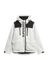 Weiße und schwarze Jacke mit Kapuze, großen Fronttaschen, zwei mit Reißverschluss versehenen Brusttaschen und einem auffälligen "SUPERDRY"-Logo auf der Vorderseite.