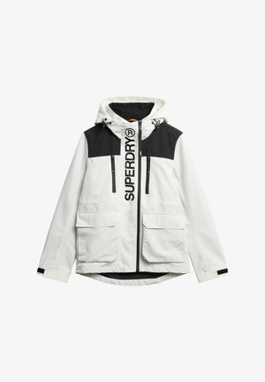 Witte en zwarte jas met capuchon, grote voorzakken, twee ritszakken op de borst en een opvallend "SUPERDRY" logo op de voorkant.