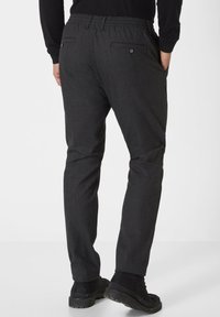 Schwarz gemusterte Hose mit bequemer Passform, ausgestattet mit einem dehnbaren Bund, zwei Rückentaschen und kombiniert mit schwarzem Schuhwerk.