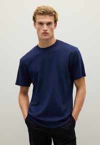 T-shirt a girocollo blu navy realizzata in tessuto liscio, con maniche corte e una vestibilità rilassata, abbinata a pantaloni scuri.
