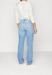 Ljust blå högmidjade jeans med rak passform, med bakfickor och kontrasterande sömmar. Klaschade med en vit tröja.