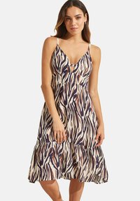 Een mouwloze jurk met dierenprint, voorzien van een diepe V-hals en een gatherings in de taille, met contrasterende strepen in marineblauw, crème en bruine tinten.