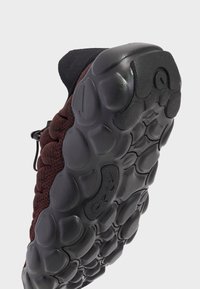 Nike shoe with a textured burgundy knit upper, black rubber sole featuring rounded patterns and grooves for traction.