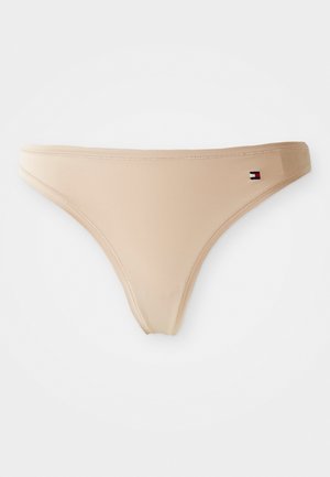 Beige seamless thong underwear with a small rectangular flag logo on the right side of the waistband.
