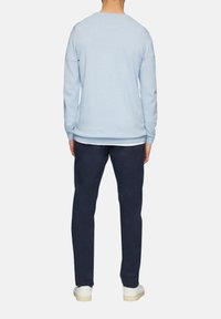 Lichtblauw pullover trui met lange mouwen, geribbelde boorden en zoom. Gedragen over navy broek en witte sneakers. Glad textuur, casual ontwerp.