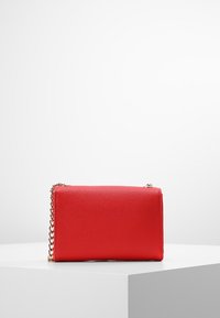 Borsa a tracolla in pelle sintetica rossa con finitura testurizzata, manico a catena dorata, forma rettangolare e chiusura con zip. Design semplice senza motivi visibili.