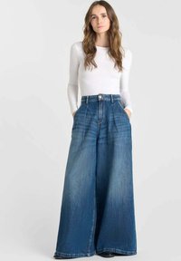 Pantalones de denim azul de pierna ancha con cintura alta, que muestran bolsillos frontales y un cierre de botón. Textura suave con un acabado desgastado.