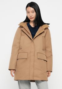 Bruine geïsoleerde parka met een capuchon, knopen aan de voorkant, twee grote voorzakken en geribbelde textuuraccenten bij de kraag.
