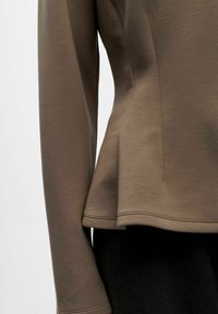 Rjav dolg rokav majica s prilegajočim pasom in razširjenim robom. Gladka tekstura, okrogla izrezana ovratnika in vidni detajli šivov.